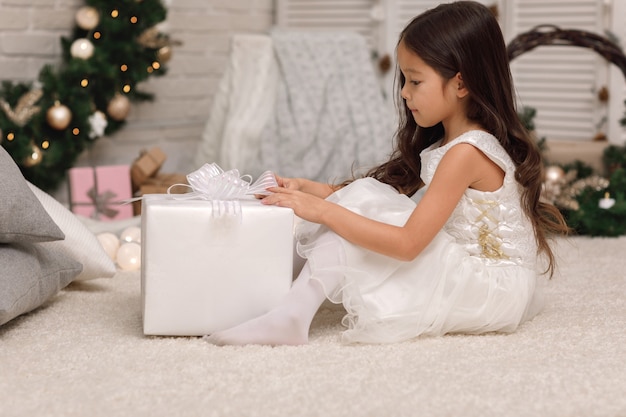 Ragazza abbastanza sorridente che apre la grande scatola con il regalo di Natale a casa