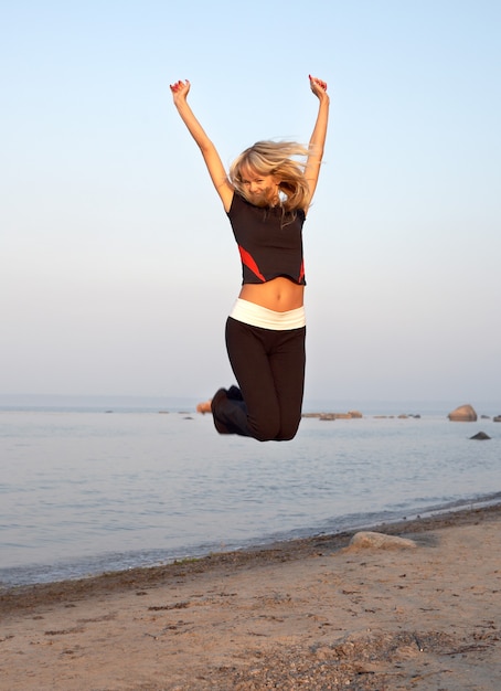 ragazza adatta che salta in riva al mare