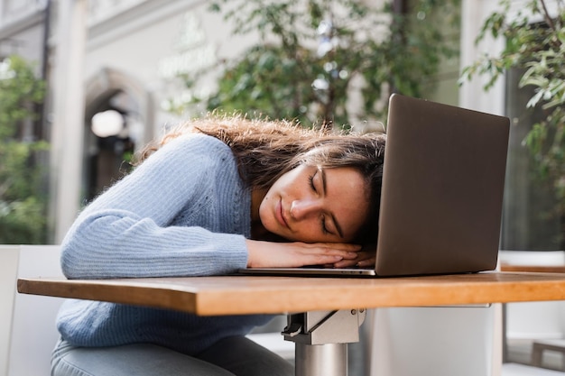 Ragazza addormentata con il computer portatile sul tavolo all'aperto nella caffetteria La giovane donna stanca si prende una pausa al lavoro e dorme e si rilassa al computer portatile sul posto di lavoro a causa del lavoro straordinario