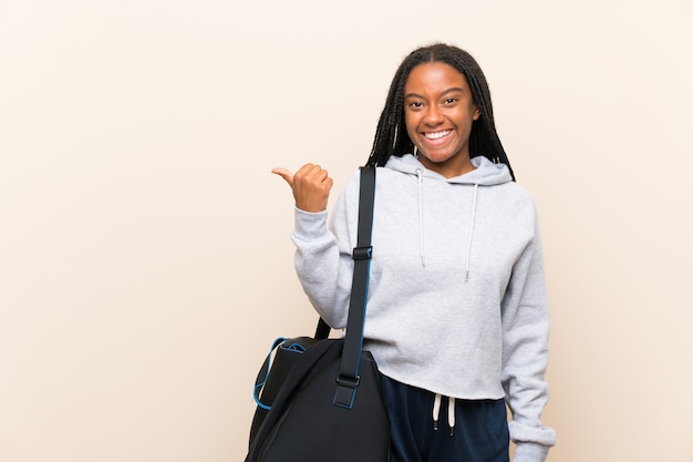 Ragazza adolescente afroamericana sportiva con lunghi capelli intrecciati che punta verso il lato per presentare un prodotto