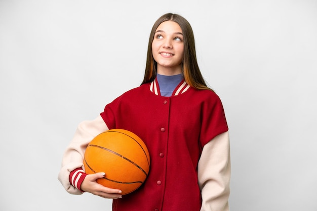 Ragazza adolescente che gioca a basket su sfondo bianco isolato pensando un'idea mentre cerca