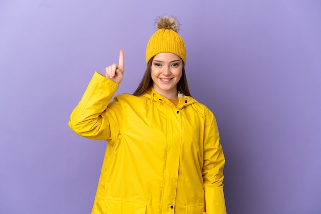Ragazza adolescente che indossa un cappotto antipioggia su sfondo viola isolato che indica una grande idea