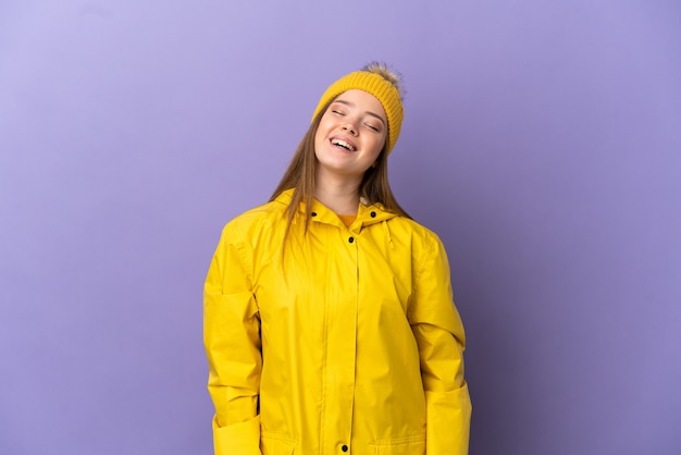 Ragazza adolescente che indossa un cappotto antipioggia su sfondo viola isolato ridendo