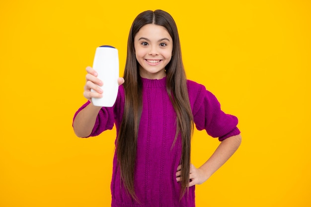 Ragazza adolescente che mostra balsami shampoo in bottiglia o gel doccia isolati su sfondo giallo Prodotto cosmetico per capelli Flacone mock up