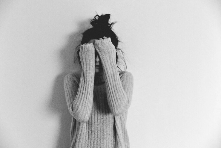 Foto ragazza adolescente che nasconde la faccia mentre sta in piedi contro uno sfondo bianco