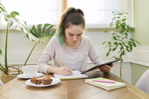 Ragazza adolescente che studia a casa, giovane studente seduto al tavolo con tablet digitale, quaderni scolastici, libri di testo. Apprendimento a distanza online, tecnologia, concetto di educazione