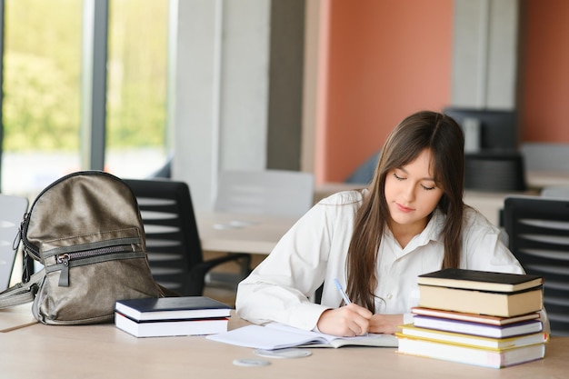 Ragazza adolescente che studia con un libro di testo scrive un saggio che impara in classe