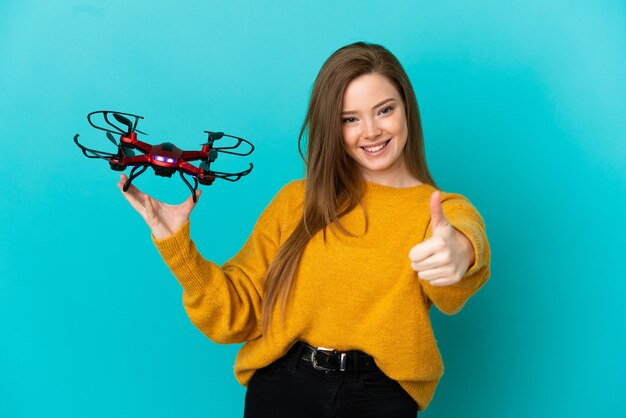 Ragazza adolescente che tiene un drone su sfondo blu isolato con il pollice in alto perché è successo qualcosa di buono