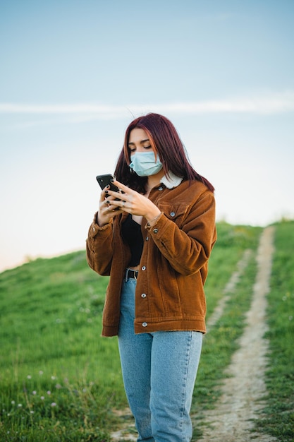 Ragazza adolescente che usa uno smartphone su un sentiero in collina Indossa una maschera facciale