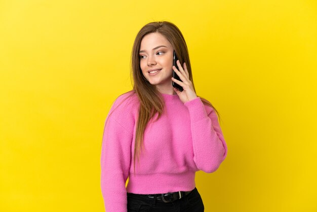 Ragazza adolescente che utilizza il telefono cellulare su sfondo giallo isolato guardando di lato e sorridente