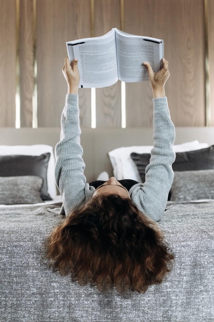 Ragazza adolescente con capelli ricci sdraiato sul letto e libro di lettura