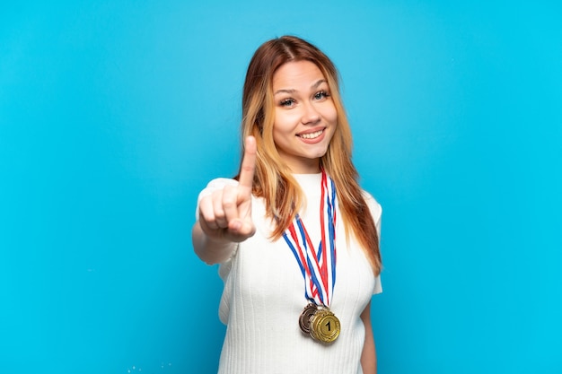 Ragazza adolescente con medaglie su sfondo isolato che mostra e solleva un dito