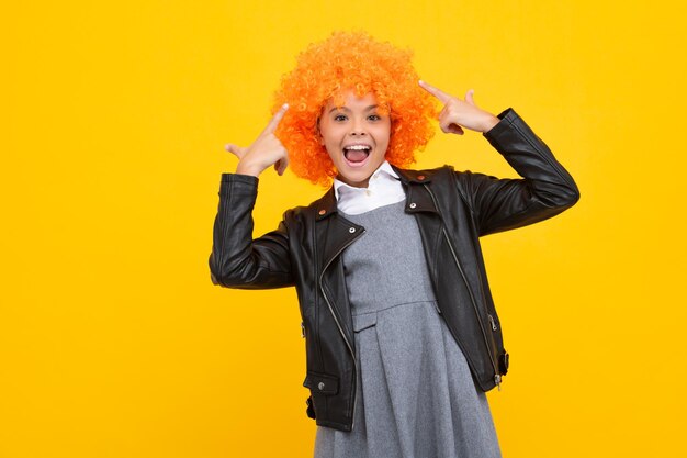 Ragazza adolescente con parrucca gialla Bambino divertente che indossa una parrucca ricci arancioni Emozioni allegre del viso eccitato della ragazza adolescente