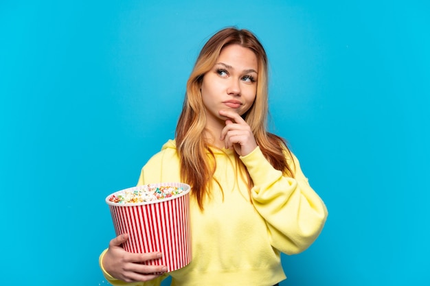 Ragazza adolescente con popcorn su sfondo blu isolato e guardando in alto