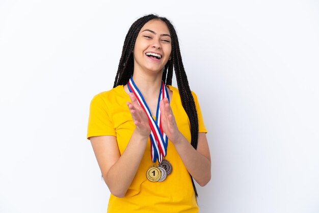 Ragazza adolescente con trecce e medaglie su sfondo rosa isolato che applaude dopo la presentazione in una conferenza