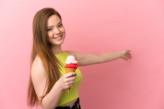 Ragazza adolescente con un gelato alla cornetta su sfondo rosa isolato che estende le mani di lato per invitare a venire