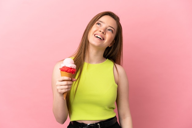 Ragazza adolescente con un gelato alla cornetta su sfondo rosa isolato ridendo