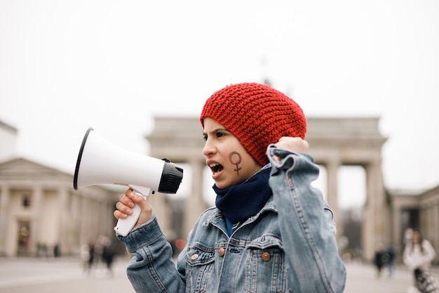 Ragazza adolescente con un simbolo femminile dipinto sul viso con un megafono in mano in una manifestazione
