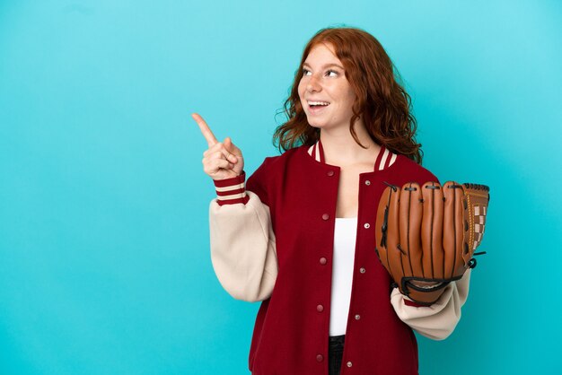 Ragazza adolescente dai capelli rossi con guanto da baseball isolato su sfondo blu con l'intenzione di realizzare la soluzione mentre si solleva un dito