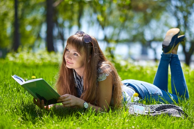 ragazza adolescente dello studente che legge un libro in parco e che si trova sull'erba