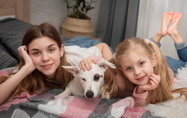 Ragazza adolescente e bambino che gioca con il loro cane jack russell sul letto di casa