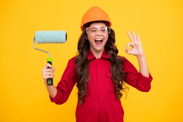 Ragazza adolescente eccitata Pittore in officina Ristrutturazione e riparazione Ragazza adolescente in casco con pennello da pittura Bambino con elmetto Pittore costruttore di bambini in cantiere