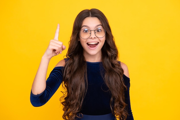 Ragazza adolescente eccitata Primo piano faccia buffa giovane adolescente che punta verso l'alto con il dito isolato su giallo