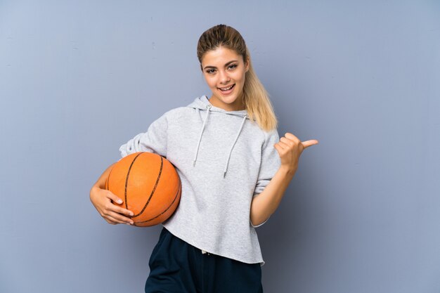 Ragazza adolescente giocando a basket muro grigio con il pollice in alto perché è successo qualcosa di buono