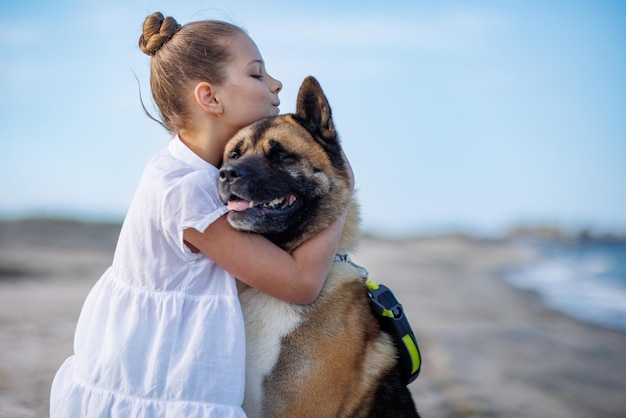 Ragazza adolescente in abiti leggeri abbraccia e ama cane amico di razza Akita Inu sulla spiaggia vicino al Mar Nero in un clima caldo e soleggiato