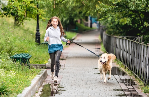 Ragazza adolescente in esecuzione con il golden retriever cane nel parco dopo la pioggia