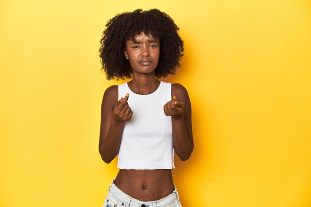 Ragazza adolescente in tank top bianco sullo sfondo giallo dello studio che mostra che non ha soldi