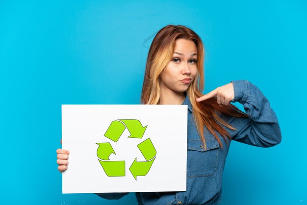 Ragazza adolescente isolata tenendo un cartello con l'icona di riciclo e indicandolo