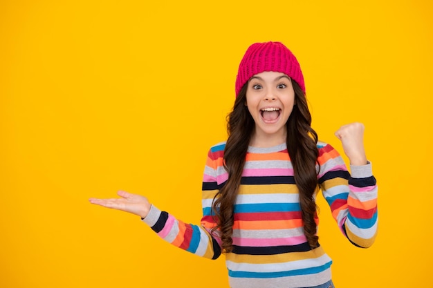 Ragazza adolescente moderna che indossa un maglione e un cappello lavorato a maglia su sfondo giallo isolato Adolescente felice emozioni positive e sorridenti della ragazza adolescente