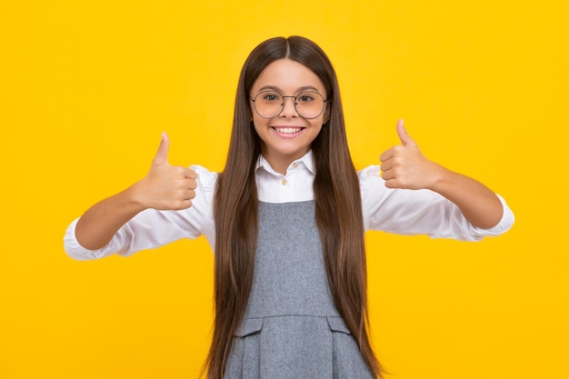 Ragazza adolescente ottimista cool con il pollice in su isolato su sfondo giallo Piccola studentessa studentessa Felice ragazza faccia emozioni positive e sorridenti