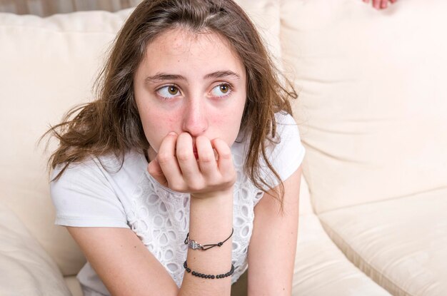 Ragazza adolescente pensierosa con la mano sul mento seduta sul divano a casa