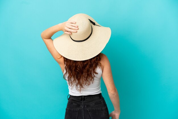 Ragazza adolescente rossa isolata su sfondo blu in costume da bagno e in posizione posteriore