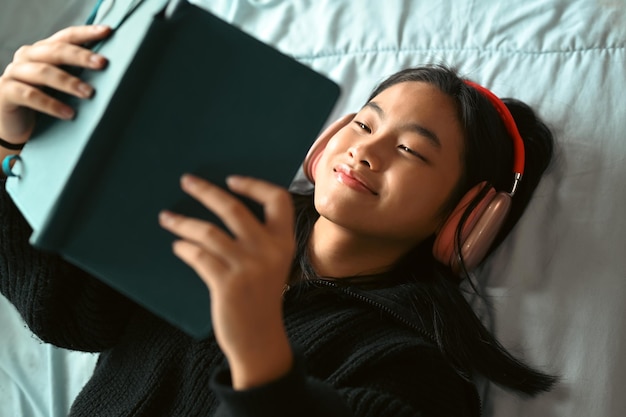 Ragazza adolescente spensierata sdraiata sul letto in una camera da letto accogliente e libro di lettura Tempo libero e concetto di persone