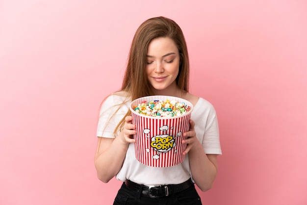 Ragazza adolescente su sfondo rosa isolato con in mano un grande secchio di popcorn