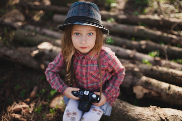 Ragazza adorabile con la macchina fotografica che si siede su legno