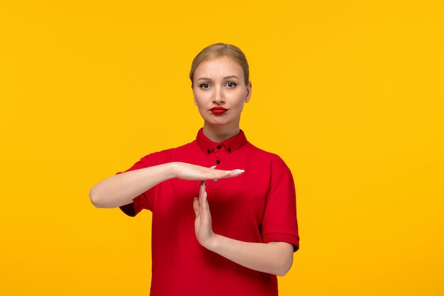 Ragazza adorabile di giorno della camicia rossa che mostra il fanale di arresto in una camicia rossa su una priorità bassa gialla