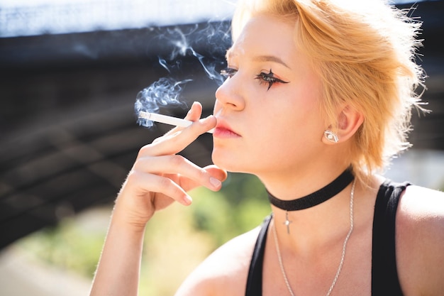 Ragazza affascinante con capelli corti e trucco che fuma una sigaretta