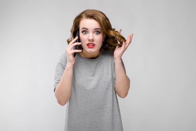 Ragazza affascinante in una maglietta grigia. La ragazza parla al telefono