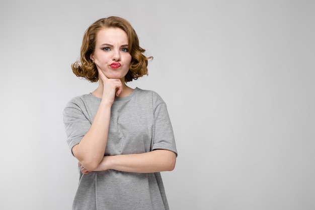 Ragazza affascinante in una maglietta grigia su un fondo grigio. La ragazza appoggiò una mano sul mento