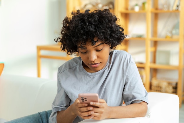 Ragazza africana che tiene lo smartphone touch screen digitando la pagina di scorrimento a casa