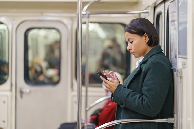 Ragazza africana dipendente dallo smartphone che scorre sui social media mentre guida in metropolitana per andare al lavoro o a casa