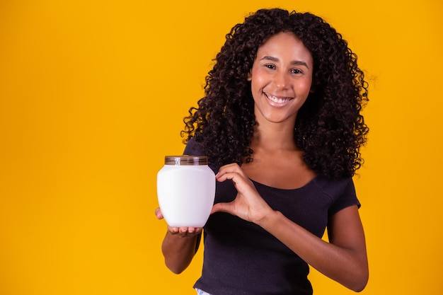 Ragazza afro carina con capelli ricci con una bottiglia di crema idratante Donna afro con maschera idratante per capelli afro