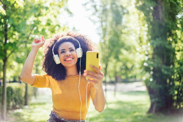 Ragazza afro che balla felice ascoltando musica con le cuffie in un parco