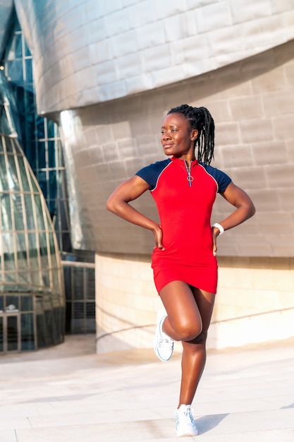 Ragazza afro nera sorridente in posa per la strada di una città moderna con un vestito rosso colorato