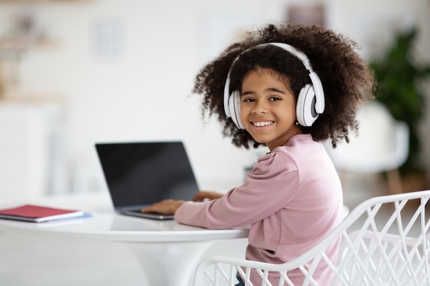 Ragazza afroamericana allegra che usa le cuffie e il modello del computer portatile