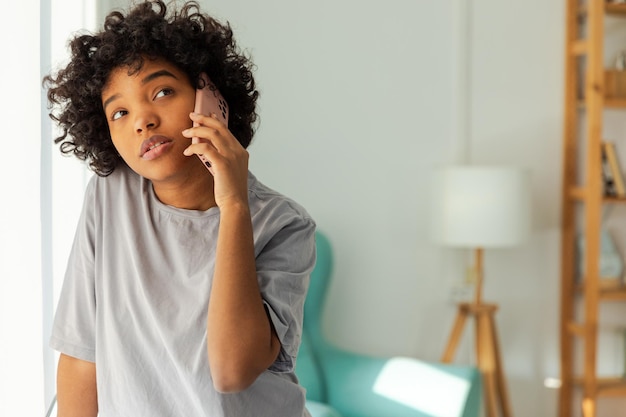 Ragazza afroamericana che parla sullo smartphone a casa giovane donna al coperto con il cellulare che chiacchiera con